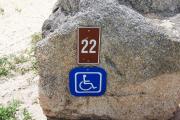 Large rock with metal sign with campsite number 22 on it located to the right of the site. Ground cover and low vegetation around rock. Handicap site.