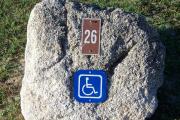 Large rock with metal sign with campsite number 26 on it located to the right of the site. Handicap site. Ground cover and low vegetation around rock.