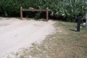 Packed sand campsite with palmetto plants and sea oats along back. Barricade posts at back to protect vegetation. Beach overlook on the left side. Walkway is non-intrusive. Electric and water hookups located on the right.