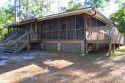 View of the front of a modern ADA compliant cabin. Stairs lead to the large screen porch. The cabin is grey with white trim and is wood frame constructed.
