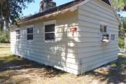 Close up of the back side of an historic cabin. The cabin is grey with white trim. These cabins are wood frame constructed with lap siding.