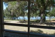 View from the porch of a historic cabin. A picnic table and fire ring is in the foreground and a line of trees and a beautiful blue lake are seen in the background.