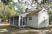 Close up of the front of an historic cabin. The cabin is grey with white trim and has a screen porch. There is a path leading to the front porch. These cabins are wood frame constructed with lap siding.