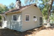 Close up of the back side of an historic cabin. The cabin is grey with white trim. These cabins are wood frame constructed with lap siding.