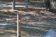 Close up of a brown campsite marker with an arrow on a wooden post. Grass is present in the foreground and an electric pedestal and a water spigot are in the background.