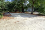View of a vacant campsite with a picnic table, fire ring, electric pedestal, and water spigot. The site has a concrete side walk and camper pad. The sidewalk leads to the campsite and to the campground restroom. There are a few trees on the edges and partial shade. This site is ADA compliant.