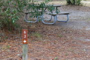 Close up of a brown site marker with an arrow on a wooden post. There is grass in the foreground and a picnic table in the background.