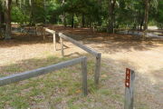 Close up of a brown site marker with an arrow on a wooden post. There are wooden barricades to the left of the marker and a picnic table is visible in the background.