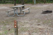 Close up of a brown site marker with an arrow on a wooden post. There is a picnic table, fire ring, and electric pedestal in the background.