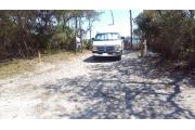 Front view of site 10 with electric and water hook-up to the right, clothesline to the left, picnic in the back.  Site is surrounded by native vegetation and trees and has a view of Western Lake. Site is dirt.