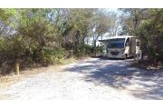 Front view of site 20 with electrical hook-up to the right, clothesline to the left, and picnic table to the rear. Site is surrounded by native vegetation with a view of Western Lake to the rear. Site is dirt.