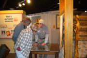 A friendly volunteer is explaining park history through an exhibit to a casually dressed man and woman in a museum.