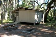 Cabin with picnic table and ground grill.