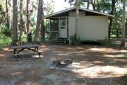Cabin with picnic table and ground grill.