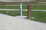 Photo: 003, Site number next to water and electric hooks ups at the back of a gravel site.