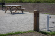 Photo: 008, Site number next to water and electric hooks ups at the back of a gravel site. A picnic table and grill sit to the left.