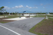 Photo: 009, ADA-accessible campsite with picnic table, grill and fire ring on the left and water and electric on the left. A paved sidewalk leads to the restroom.