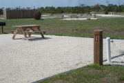 Photo: 033, - Site number next to water and electric hooks ups at the back of a gravel site. A picnic table can be seen to the left.