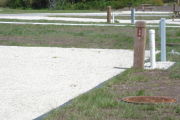 Photo: 034, Site number next to water and electric hooks ups at the back of a gravel site.