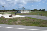 Photo: 036, ADA-accessible campsite with picnic table, grill and fire ring on the left and water and electric on the left. A paved sidewalk leads to a nearby restroom.