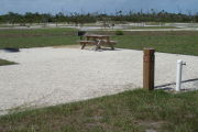 Photo: 039, Site number next to water and electric hooks ups at the back of a gravel site. A picnic table, grill and fire ring can be seen to the left.