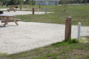 Photo: 042, Site number next to water and electric hooks ups at the back of a gravel site. A restroom is nearby.