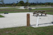 Photo: 043, Site number next to water and electric hooks ups at the back of a gravel site. A picnic table, grill and fire ring can be seen to the left.