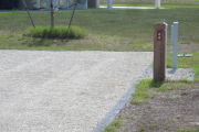 Photo: 044, Site number next to water and electric hooks ups at the back of a gravel site. A restroom is nearby.