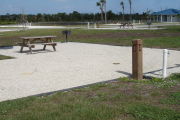 Photo: 045, Site number next to water and electric hooks ups at the back of a gravel site. A restroom is nearby. A picnic table, grill and fire ring can be seen to the left.