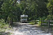 A small motor home sits squarely on campsite number ten as bright sunlight filters through the dense green oak tree canopy, decorating the dirt and gravel pad at Lake Griffin State Park