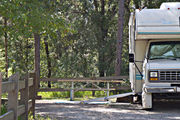 A small motor home sits squarely on campsite number ten, adjacent to a picnic table and rustic wooden fencing, at Lake Griffin State Park