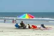 A colorful umbrella shading a family at Little Talbot Island State Park beach with other people sun bathing and enjoying the water.