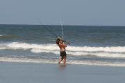Woman surf fishing with her pole flexing as she reels in her catch through the crashing waves.