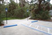 Lush vegetation of Spanish moss draped live oak, sable palm, cedar, and palmetto surrounding two Accessible parking spaces with walkway to the bathhouse.