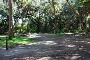 Campsite 2 is a partial sunny site with a gravel foundation located on the right hand side of the road.  Looking into the site on the right is the water and 50amp electrical service. There is a picnic table and ground campfire ring.  At the front left side of the site is the brown site marker.
