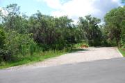 This picture of campsite #49 is looking from the road into the sunny site.  This site has 50 amp electric, water and sewer hook-ups. There is a stone foundation with vegetation on the sides.  There is also a separate area to the side with a picnic table, cooking grill and ground campfire ring.