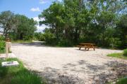 This is picture of campsite #51 from the back of the site looking toward the road.  Site has 50amp electric, water and sewage hook-ups.  This is a sunny site with stone foundation and vegetation on sides.  There is a separate section to the side with the picnic table, cooking grill and ground campfire ring.