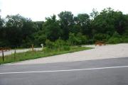 This picture of campsite #55 is looking from the road into the sunny site.  This site has 50 amp electric, water and sewer hook-ups. There is a stone foundation with vegetation on the sides.  There is also a separate area to the side with a picnic table, cooking grill and ground campfire ring.