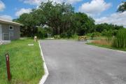 This picture of campsite #61 is looking from the road into the sunny site.  This is an ADA accessible site that has 50 amp electric, water and sewer hook-ups. There is an asphalt foundation with vegetation on the sides.  There is also a separate area to the side with a picnic table, cooking grill and ground campfire ring.  Next to the site is a sidewalk with easy access to the restroom.  This site has to be pulled straight into.