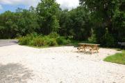 This is picture of campsite #71 from the back of the site looking toward the road.  Site has 50amp electric, water and sewage hook-ups.  This is a sunny site with stone foundation and vegetation on sides.  There is a separate section to the side with the picnic table, cooking grill and ground campfire ring.