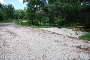 This is picture of campsite #75 from the back of the site looking toward the road.  Site has 50amp electric, water and sewage hook-ups.  This is a sunny site with stone foundation and vegetation on sides.  There is a separate section to the side with the picnic table, cooking grill and ground campfire ring.