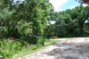 This picture of campsite #75 is looking from the road into the sunny site.  This site has 50 amp electric, water and sewer hook-ups. There is a stone foundation with vegetation on the sides.  There is also a separate area to the side with a picnic table, cooking grill and ground campfire ring.