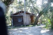 This is a front view picture of Cabin 1 which is a rustic palm log cabin built by the Civilian Conservation Corp. in the mid 1930âs.  This cabin is ADA accessible.  There is a living/dining/bedroom area with 2 double beds, a sofa bed, dining set, linen cabinet and fireplace.  There also is a bathroom and a kitchen with coffee maker, toaster, microwave, range, refrigerator, dishes, silverware and cooking utensils.  The cabins sleep up to six. Off of the back porch, there is a fire ring, cooking grill and a picnic table.  There are no pets and no smoking allowed in the cabins.