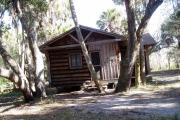 This is a front view picture of Cabin 2 which is a rustic palm log cabin built by the Civilian Conservation Corp. in the mid 1930âs.  There is a living/dining/bedroom area with 2 double beds, a sofa bed, dining set, linen cabinet and fireplace.  There also is a bathroom and a kitchen with coffee maker, toaster, microwave, range, refrigerator, dishes, silverware and cooking utensils.  The cabins sleep up to six.  Off of the back porch, there is a fire ring, cooking grill and a picnic table.  There are no pets and no smoking allowed in the cabins.