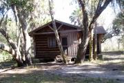 This is a front view picture of Cabin 2 which is a rustic palm log cabin built by the Civilian Conservation Corp. in the mid 1930âs.  There is a living/dining/bedroom area with 2 double beds, a sofa bed, dining set, linen cabinet and fireplace.  There also is a bathroom and a kitchen with coffee maker, toaster, microwave, range, refrigerator, dishes, silverware and cooking utensils.  The cabins sleep up to six.  Off of the back porch there is a fire ring, cooking grill and a picnic table.  There are no pets and no smoking allowed in the cabins.