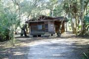 This is a front view picture of Cabin 3 which is a rustic palm log cabin built by the Civilian Conservation Corp. in the mid 1930âs.  There is a living/dining/bedroom area with 2 double beds, a sofa bed, dining set, linen cabinet and fireplace.  There also is a bathroom and a kitchen with coffee maker, toaster, microwave, range, refrigerator, dishes, silverware and cooking utensils.  The cabins sleep up to six.  Off of the back porch there is a fire ring, cooking grill and a picnic table.  There are no pets and no smoking allowed in the cabins.