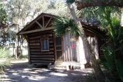 This is a front view picture of Cabin 4 which is a rustic palm log cabin built by the Civilian Conservation Corp. in the mid 1930âs.  There is a living/dining/bedroom area with 2 double beds, a sofa bed, dining set, linen cabinet and fireplace.  There also is a bathroom and a kitchen with coffee maker, toaster, microwave, range, refrigerator, dishes, silverware and cooking utensils.  The cabins sleep up to six.  Off of the back porch there is a fire ring, cooking grill and a picnic table.  There are no pets and no smoking allowed in the cabins.
