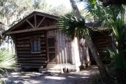 This is a front view picture of Cabin 4 which is a rustic palm log cabin built by the Civilian Conservation Corp. in the mid 1930âs.  There is a living/dining/bedroom area with 2 double beds, a sofa bed, dining set, linen cabinet and fireplace.  There also is a bathroom and a kitchen with coffee maker, toaster, microwave, range, refrigerator, dishes, silverware and cooking utensils.  The cabins sleep up to six.  Off of the back porch there is a fire ring, cooking grill and a picnic table.  There are no pets and no smoking allowed in the cabins.