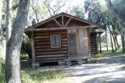This is a front view picture of Cabin 5 which is a rustic palm log cabin built by the Civilian Conservation Corp. in the mid 1930âs.  There is a living/dining/bedroom area with 2 double beds, a sofa bed, dining set, linen cabinet and fireplace.  There also is a bathroom and a kitchen with coffee maker, toaster, microwave, range, refrigerator, dishes, silverware and cooking utensils.  The cabins sleep up to six.  Off of the back porch there is a fire ring, cooking grill and a picnic table.  There are no pets and no smoking allowed in the cabins.