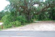 This picture of campsite #78 is looking from the road into the partial shady site.  This site has 50 amp electric, water and sewer hook-ups. There is a stone foundation with vegetation on the sides.  There is also a separate area to the side with a picnic table, cooking grill and ground campfire ring.